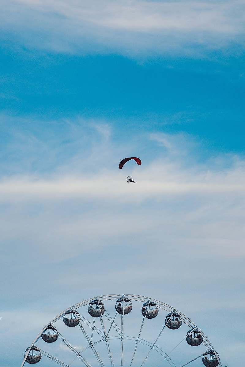 ferris wheel aerial photography of person parachuting above ferris wheel amusement park
